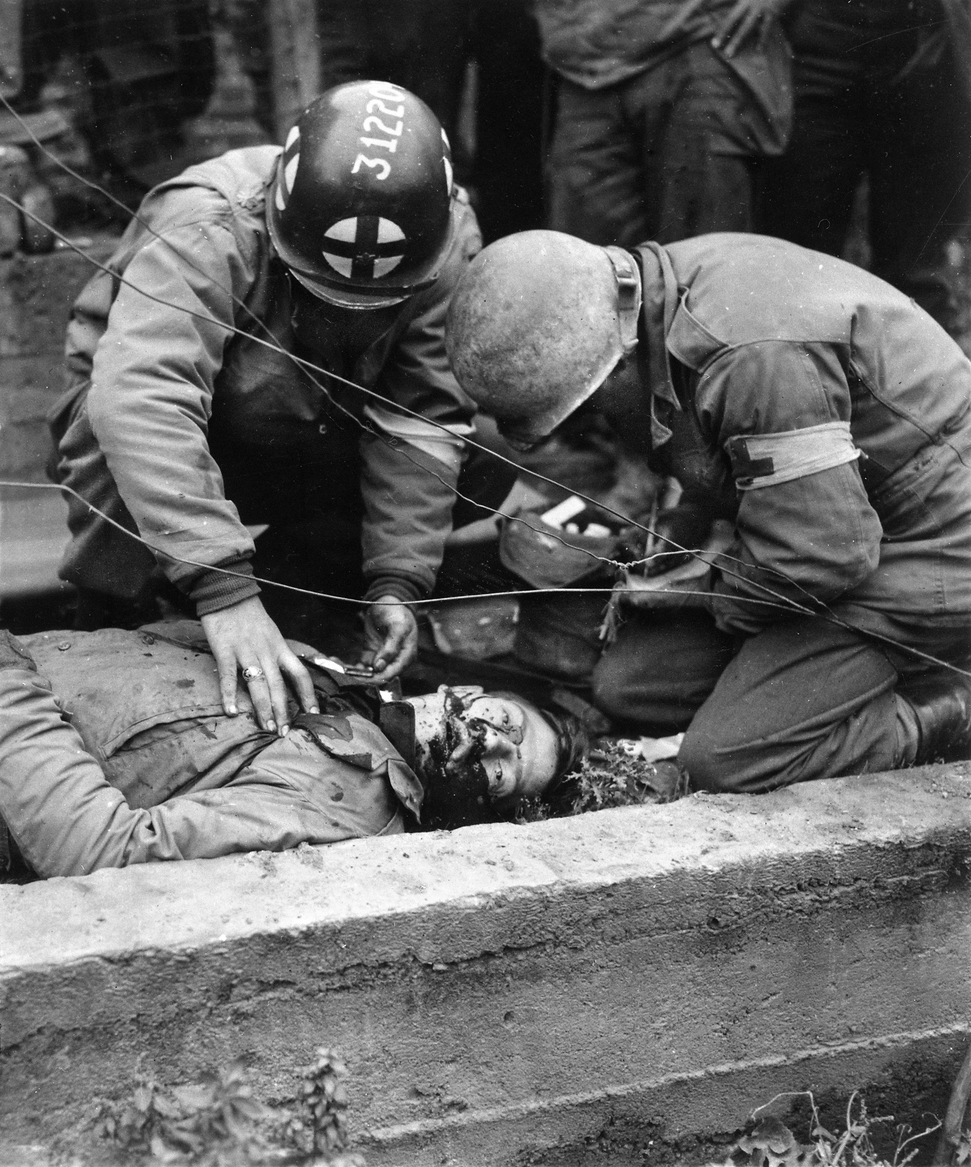 Two medics who have worked unsuccessfully to save an American soldier killed during the Battle of the Hürtgen Forest check his tags for identification, October 1944. The battle, one of the most difficult ever fought by the U.S. Army, resulted in the decimation of several divisions and heavy American casualties.